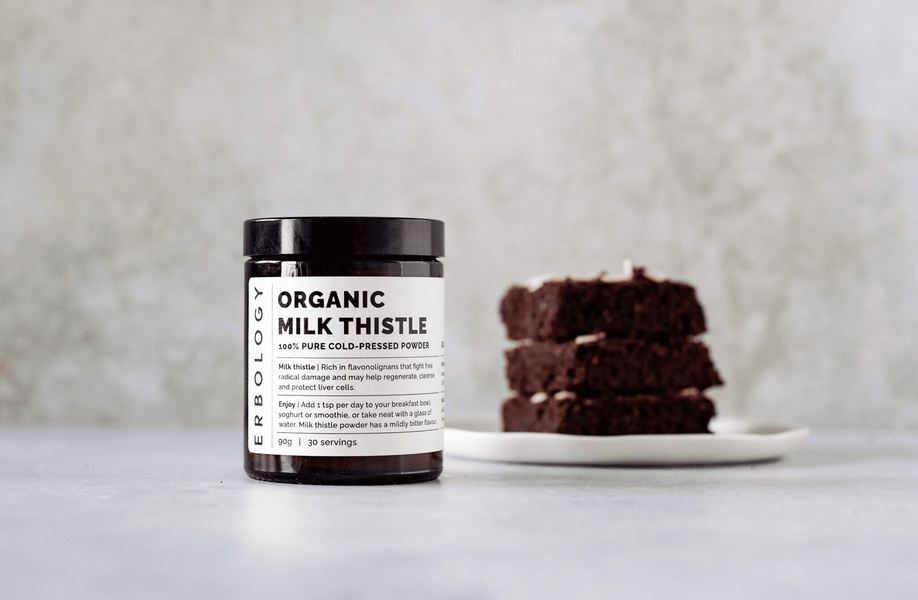 A clean, high-contrast studio shot featuring a single jar of organic milk thistle powder beside a plate of brownies, emphasizing natural usage.